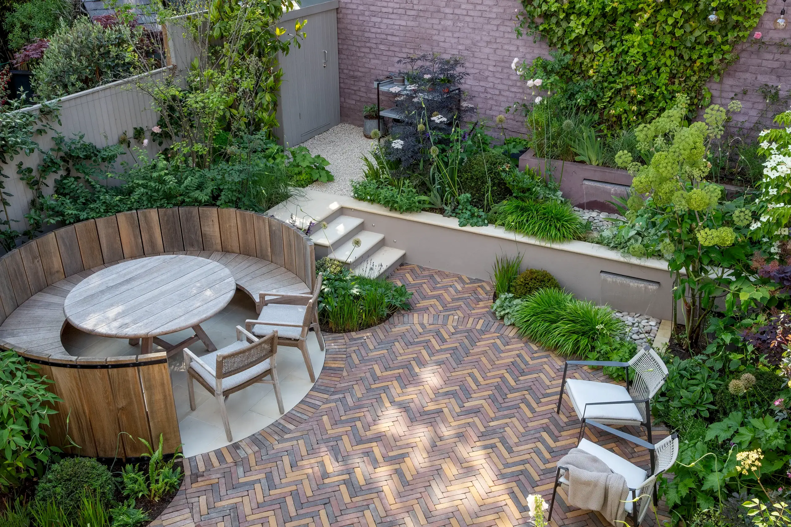 Garden design on two levels in North London with brick paving and circular bench, water feature and planting