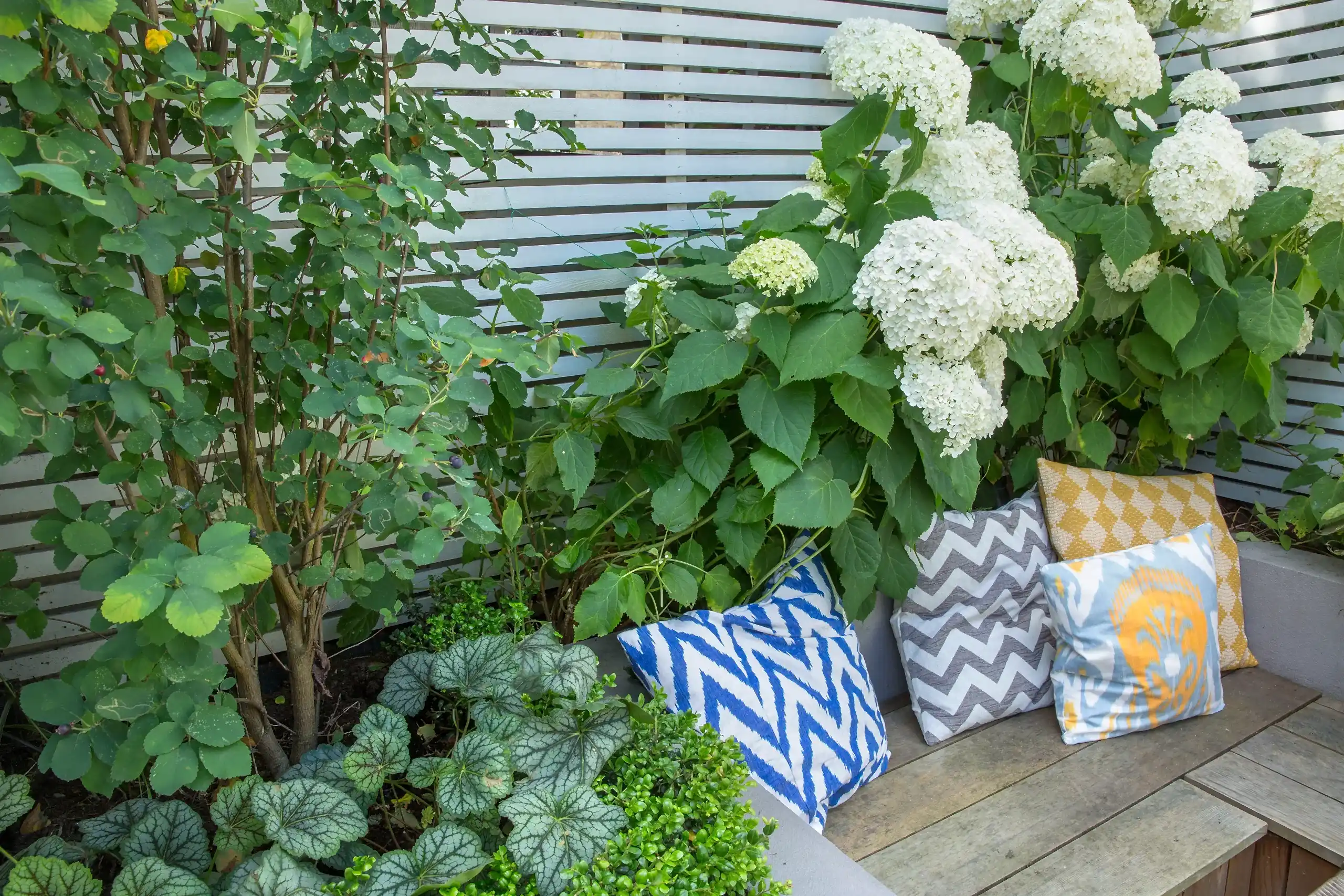 a bench with pillows and plants in front of a white fence