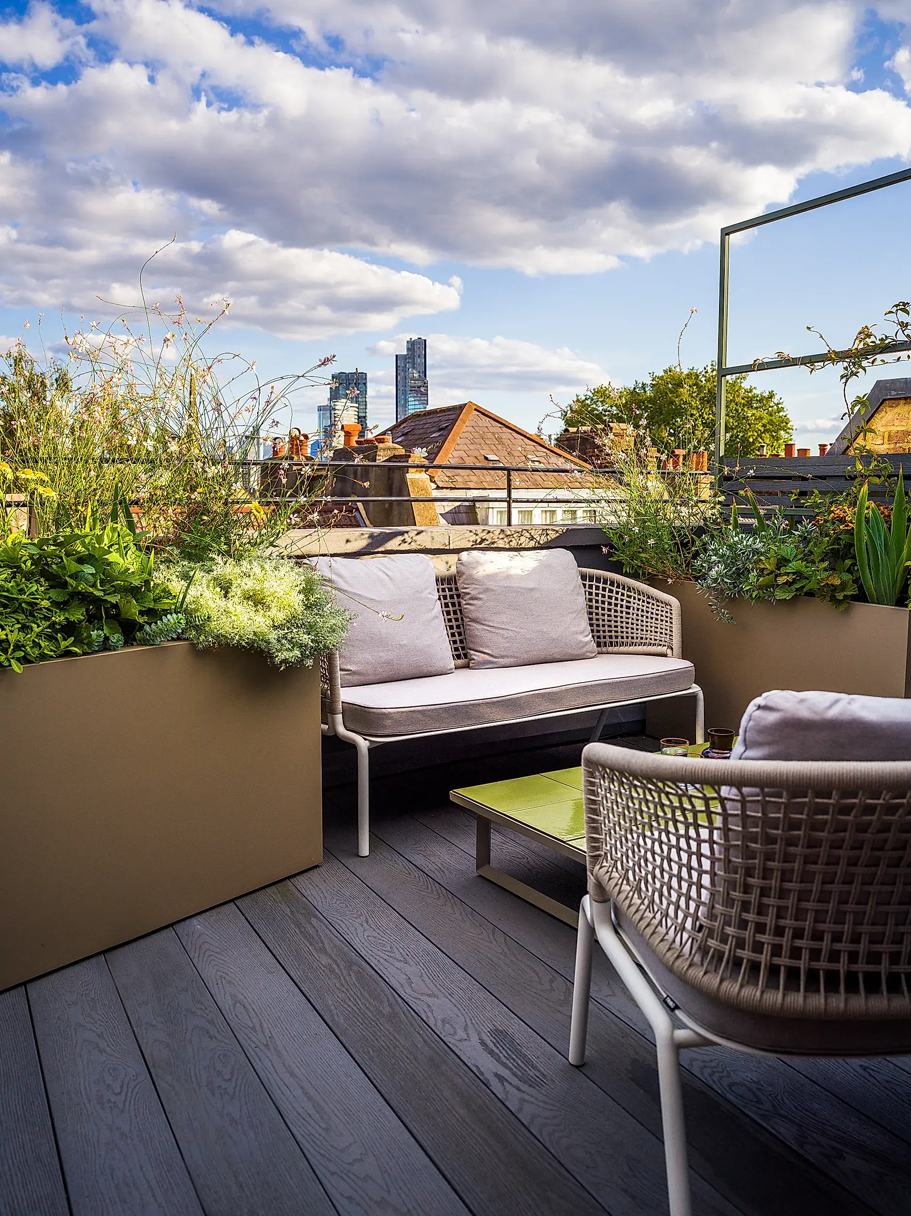 London roof terrace showcases new furniture as part of an outdoor revival. Cream coloured seating is set between overflowing planters centred with an olive green tiled coffee table.