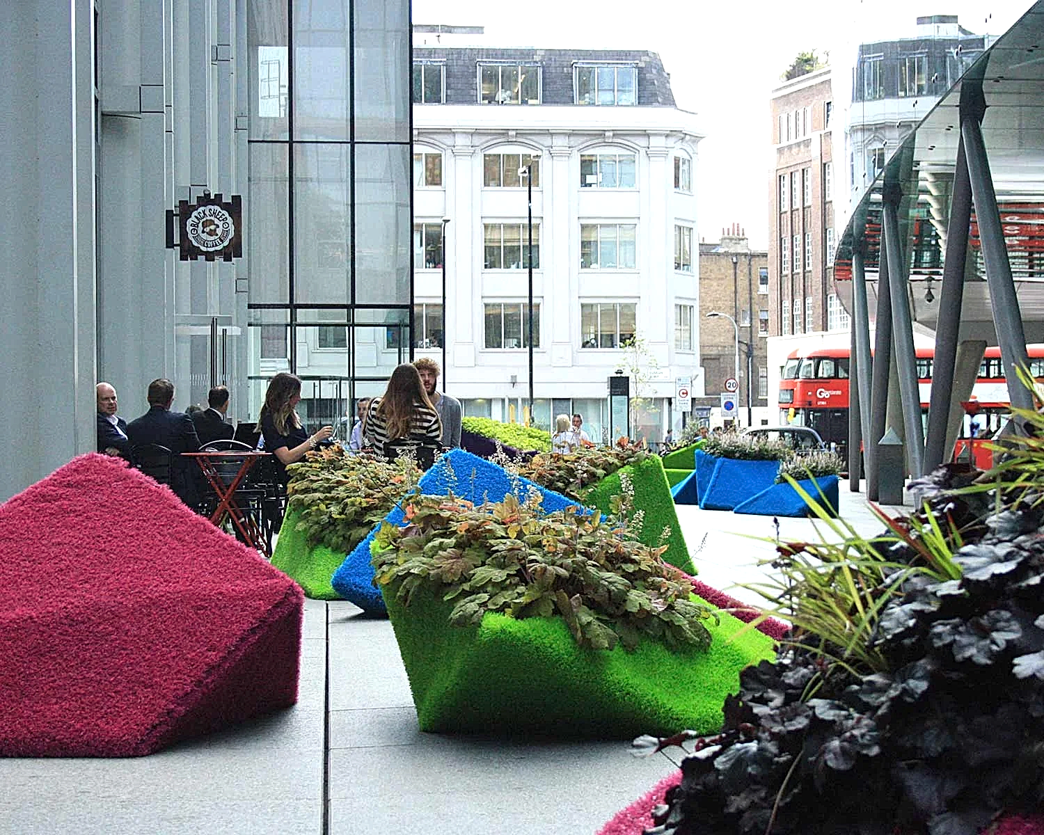 people sitting outside a building with plants in them